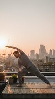 Young athletic man practicing yoga stretching exercise on urban rooftop terrace at golden hour sunset with city skyline background for wellness lifestyle.