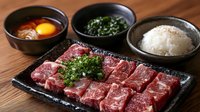Raw marbled beef cuts arranged on black stone plate with fresh herbs, served alongside rice, soup and side dishes on wooden table.