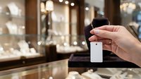 Woman's hand holding blank white price tag or label in luxury jewelry store with illuminated display cases and shelves in background, retail merchandising and pricing concept.