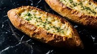 Freshly baked garlic bread with melted cheese and herbs on dark marble surface. Homemade appetizer ready for serving at dinner or restaurant meal.