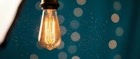 Vintage Edison bulb glowing against teal background with bokeh lights, suitable for energy, innovation, and creative concept designs.