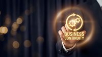Businessman holding glowing neon sign with gears and business continuity text, representing disaster recovery planning and operational resilience strategy for enterprises.