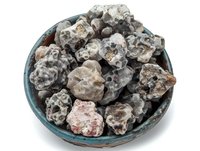 Raw geodes and mineral specimens displayed in turquoise ceramic bowl showing natural crystalline formations and rough stone textures against white background.