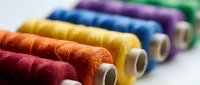Colorful sewing thread spools arranged in row showing vibrant cotton threads for crafting, tailoring and textile work on white background.