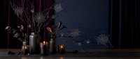 Dark moody still life with bare branches in vase, glowing candles creating warm ambient lighting against deep blue wall for home decor and interior design.