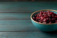 Dried cranberries in turquoise ceramic bowl on rustic wooden table background for healthy snacking and cooking ingredients.