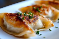Pan-seared dumplings with crispy golden-brown bottom, garnished with fresh chopped herbs on white ceramic plate, close-up view of Asian cuisine.