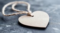 Wooden heart shape pendant with natural twine string on textured gray surface. Close-up view captures rustic charm and minimalist Valentine's day or love concept.