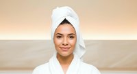 Young woman with olive skin tone wearing white bathrobe and towel wrap after shower or spa treatment, suitable for wellness, beauty and skincare marketing materials.