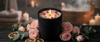 Luxury spa candle with floating rose petals in black bowl surrounded by pink roses and eucalyptus creating romantic wellness atmosphere for relaxation.