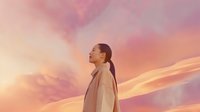 Young Asian woman with ponytail in beige coat standing against dramatic pink and orange sunset sky with clouds, side view profile expressing serenity and freedom.