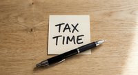 Tax time reminder note with black pen on wooden desk surface for financial planning and accounting preparation.