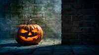Carved jack-o-lantern with glowing face sits against weathered brick wall in moody lighting, perfect for autumn and holiday marketing materials.