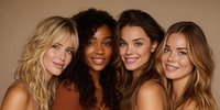 Four diverse young women with glowing skin and natural makeup posing together against warm beige background for beauty and skincare campaigns.