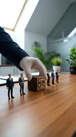 Business hand placing wooden block with justice scales symbol near miniature businessmen figures on office desk representing legal consulting services.