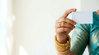 Woman with medium skin tone wearing gold jewelry and teal clothing holds blank white card for business, marketing, or promotional messaging.