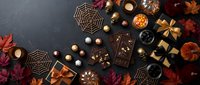 Halloween chocolate treats and autumn decorations arranged on dark background with spider web cookies, pumpkins, fall leaves and golden gift boxes.