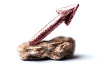 Red metallic arrow pointing upward on natural stone against white background, symbolizing growth, progress and financial success in business concept.