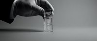 Gloved hand holding clear glass vial or test tube in laboratory setting, suitable for medical, pharmaceutical, scientific research, and healthcare industry applications.
