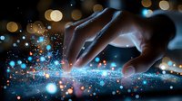 Fingers touching digital surface with glowing blue particles and bokeh lights creating magical technology interaction effect in dark environment.