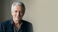Senior man with gray hair and facial stubble wearing dark casual shirt, smiling at camera against neutral background. Suitable for business, healthcare, lifestyle and corporate projects.