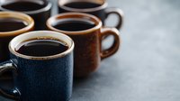 Ceramic coffee mugs filled with fresh black coffee arranged in row on dark background, selective focus on front cup creates moody atmosphere for cafe menu design.