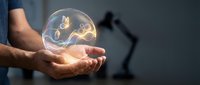 Male hands holding glowing transparent sphere with golden plant sprout inside symbolizing growth, innovation and environmental protection in modern office.