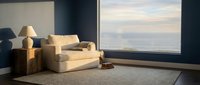 Cozy living room with beige sofa, armchair, and table lamp near large window overlooking cityscape at sunset, modern interior design space.