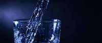 Water pouring into glass against dark background, splashing and creating dynamic motion. Refreshing beverage concept for advertising and wellness campaigns.