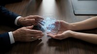 Two people exchanging glowing digital cube with data network visualization between hands at wooden desk, representing technology transfer, business collaboration, and digital innovation in corporate environment.