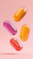 Colorful transparent gel capsules floating on pink background. Nutritional supplements and vitamins in orange, red and purple colors with sparkly texture.