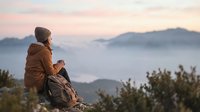 Father and son sitting on rocky mountain overlook at sunrise, gazing at misty valley landscape below. Outdoor adventure and bonding moment.