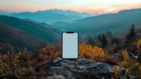 Smartphone mockup on rocky mountain peak at sunset, blank screen against scenic mountain landscape with golden autumn foliage and misty valleys.