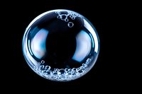 Transparent soap bubble with water droplets floating against black background for creative design projects and advertising campaigns.