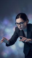 Young Caucasian businesswoman in glasses and suit interacting with virtual interface, glowing bokeh lights on dark background.