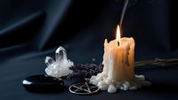 Burning candle with melted wax, crystal quartz, pentagram and ritual items on dark surface creating mystical witchcraft atmosphere for spiritual practices.