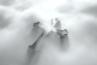 Glowing silver cross with soft edges emerges from ethereal misty background, radiating divine light and spiritual atmosphere in monochromatic grayscale tones.