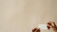 Hands holding blank white card against neutral beige background for business branding and marketing mockup designs.