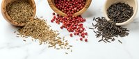 Assorted spices and seeds in wooden bowls scattered on white surface for culinary cooking and seasoning recipes.