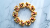 Elegant appetizer tartlets arranged in circle with prosciutto and greens on marble surface for catering and party food presentation.