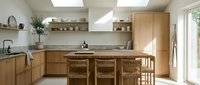 Modern Scandinavian kitchen interior with light wood cabinets, marble countertops, breakfast bar with wooden stools, and natural lighting from skylights.