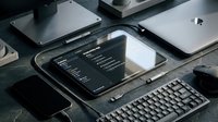 Dark workspace setup with tablet displaying analytics dashboard, surrounded by laptop, keyboard, mouse, and accessories on stone surface.