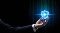 Businessman hand holding glowing shield icon with digital matrix code background for cybersecurity and data protection concept in corporate environment.
