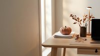 Cozy autumn workspace with pumpkin decoration on wooden desk near window with warm natural light creating peaceful home office atmosphere.