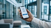 Man's hand holding smartphone with online shopping app showing buy now button in modern office lobby.