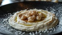 Creamy hummus dip with chickpeas and olive oil drizzle served on dark plate, Middle Eastern appetizer ready for healthy snacking and Mediterranean cuisine.