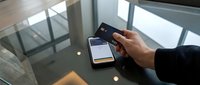Man holding credit card and smartphone over glass table, mobile banking and contactless payment concept in modern setting.