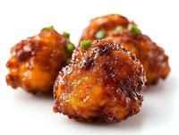 Glazed chicken wings with sweet and spicy sauce garnished with fresh green onions on white background, close-up view showing caramelized coating and juicy texture.