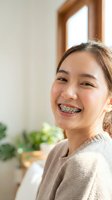 Happy young Asian woman with dental braces smiling confidently at home showing orthodontic treatment progress in bright natural light interior setting.