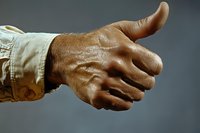 Close up of African American male hand giving thumbs up gesture against gray background, wearing beige work sleeve, showing confidence and approval.